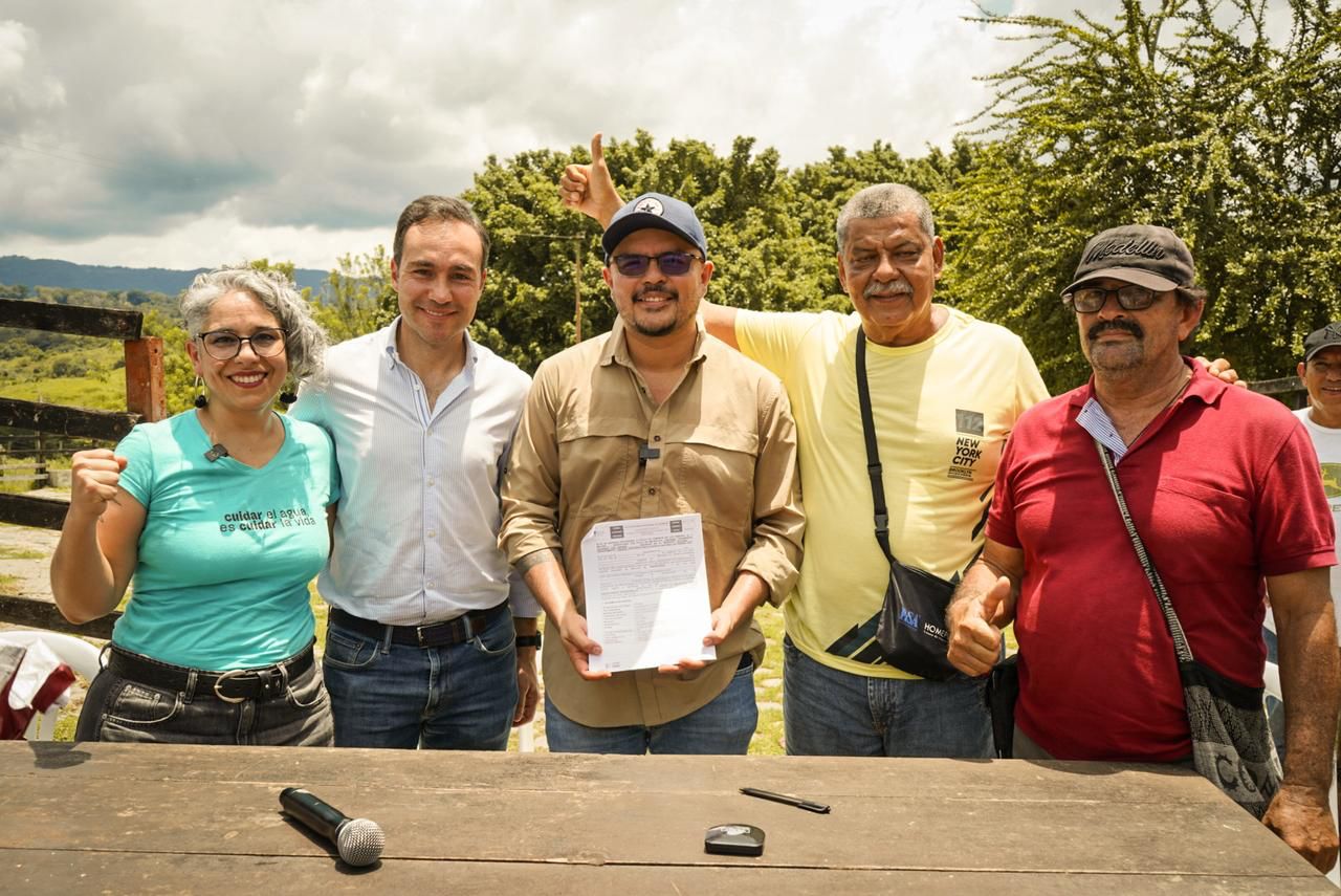 un-grupo-de-campesinos-parados-alrededor-de-una-mesa-con-un-documento-junto-director-ant