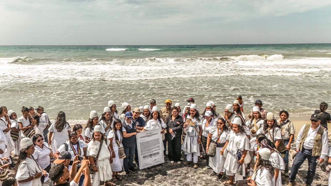 un-grupo-de-personas-paradas-en-la-playa-con-un-cartel