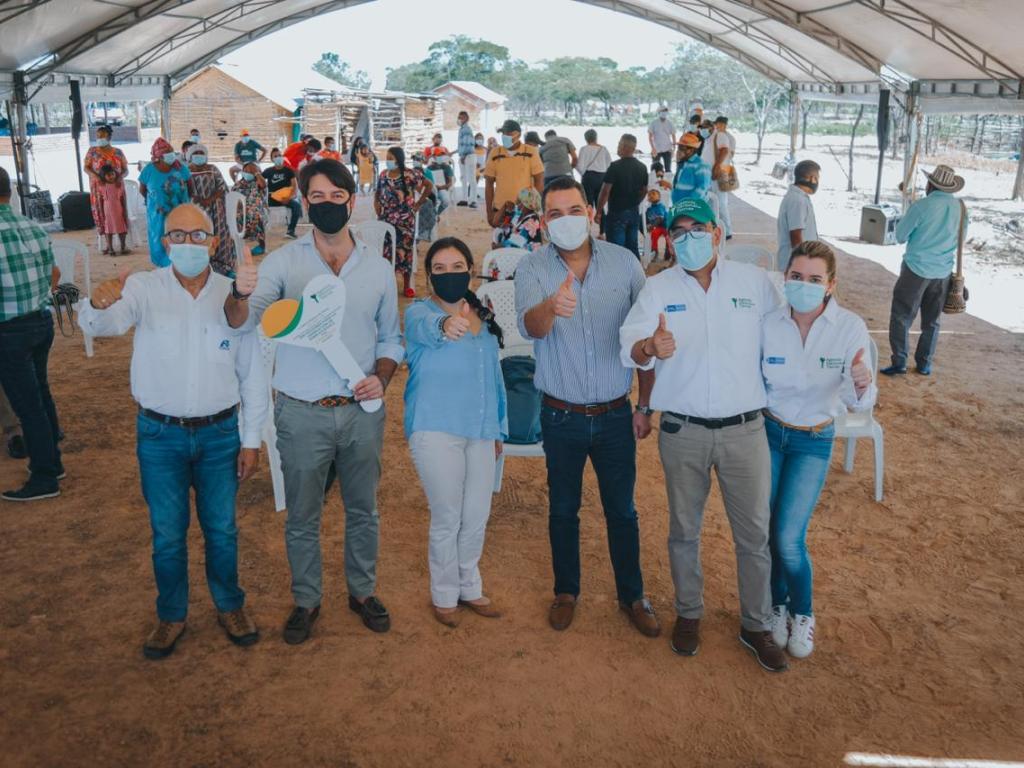 La Directora de la ANT, Myriam Martínez Cárdenas, en compañía de cuatro funcionarios de la ANT y de un beneficiario de títulos posan en alineados, cada uno con su brazo levantado y pulgar arriba. De fondo varios integrantes de un resguardo de la comunidad Wayúu.