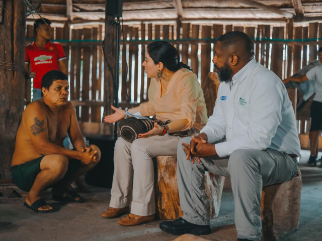 Aparece la Directora de la ANT en compañía de un funcionario de la ANT sentados sobre troncos de madera y hablando con una persona de un resguardo indígena, de la estructura de una casa en madera  y dos campesinos más cada uno a un costado.