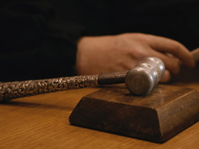 Aparece el martillo de un juez y al lado la mano del juez sosteniendo una hoja.