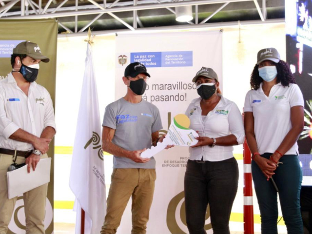 Tres funcionarios de la ANT, dos mujeres y un hombre, hacen entrega a un profesor de la Institución Educativa Rural de Pavarandóde, de una llave grande de la ANT como símbolo de la legalidad de este predio.