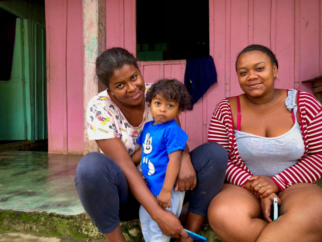 Dos mujeres y un niño pequeño, sentados afuera de su casa.