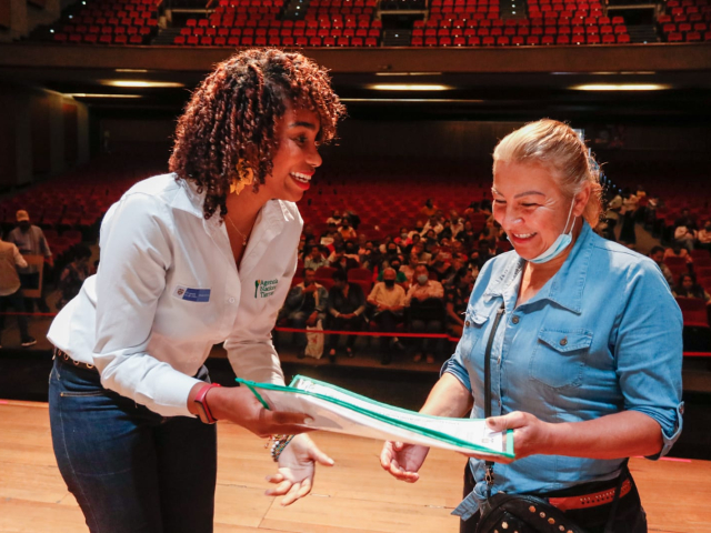 Funcionaria de la ANT entregando titulo a campesina en auditorio de Manizales