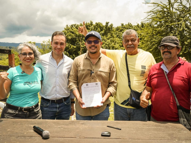un-grupo-de-campesinos-parados-alrededor-de-una-mesa-con-un-documento-junto-director-ant
