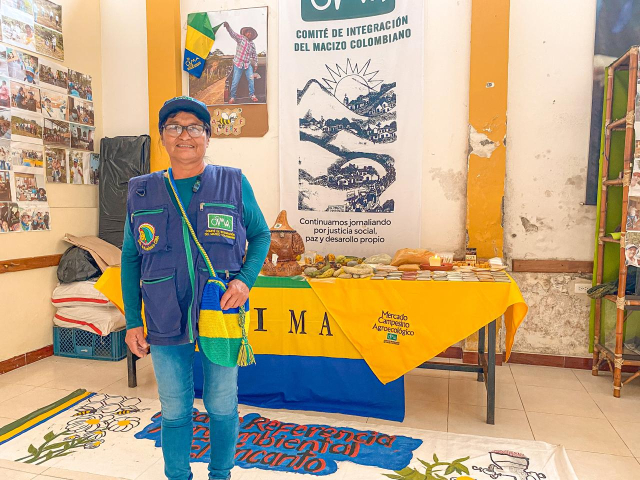 mujer-sonriendo-al-lado-de-una-mesa-con-productos-del-mercado-campesino