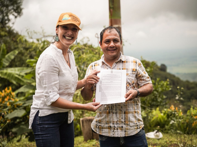 un-hombre-y-una-mujer-parados-frente-a-una-montana-sosteniendo-titulo-de-tierras