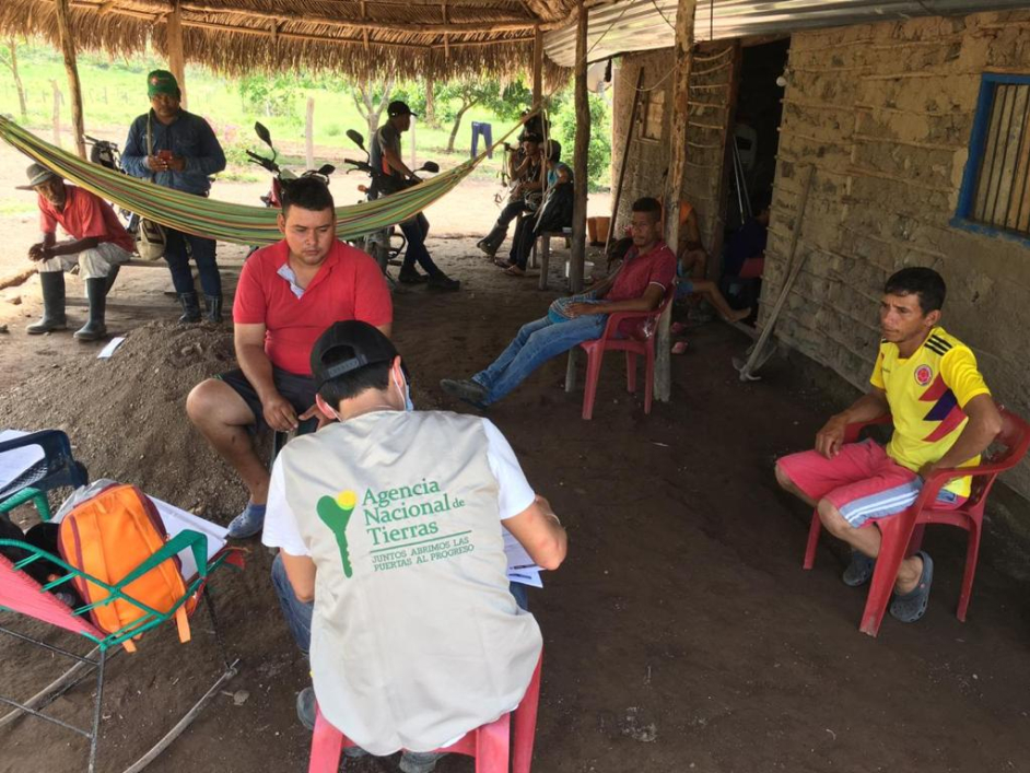Se ve a una funcionaria de la ANT, sentada en silla de plástico mientras conversa y toma datos de los campesinos, principalmente a tres de ellos. Aproximadamente habla principalmente