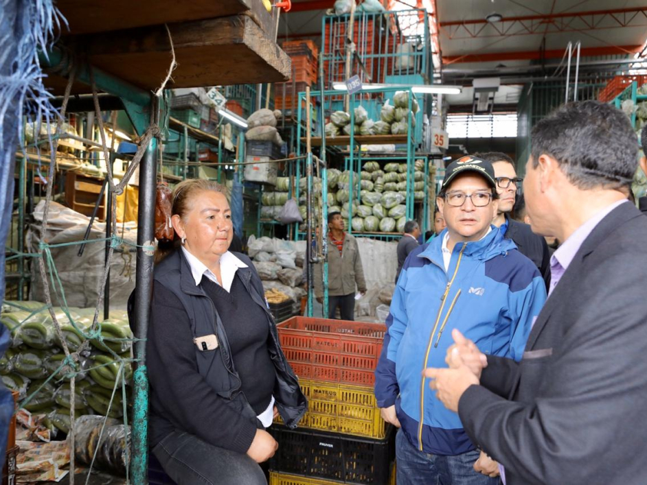 El Ministro de Agricultura, aparece con comerciantes de una plaza de mercado. De fondo se ven los alimentos que se comercializan.