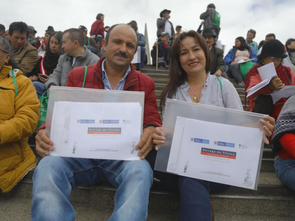 Un hombre y una mujer, felices al recibir cada uno sus títulos de propiedad y al rededor de ellos varios beneficiarios más del municipio de Ovejas.
