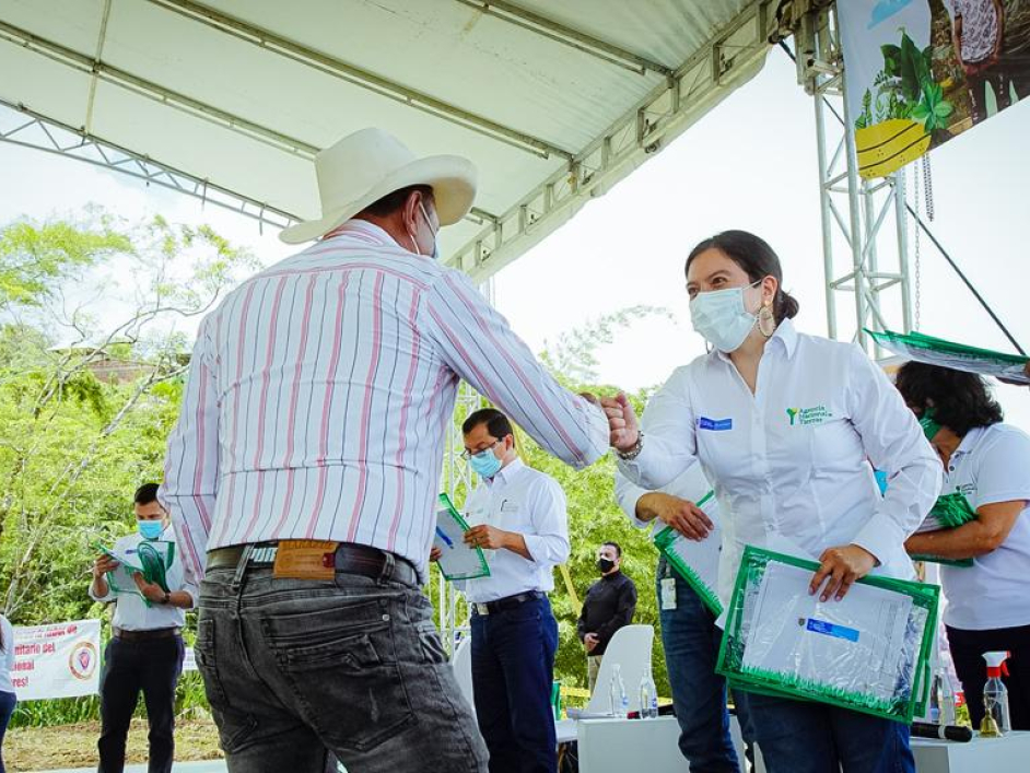 Directora de la ANT, saluda a un campesino de la mano y hace entrega del título de propiedad de un predio. Al rededor, mas funcionarios de la agencia.